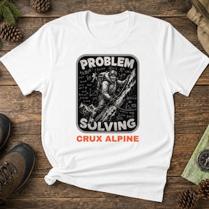 May include: A white short-sleeve t-shirt featuring a black and white graphic of a mountaineer climbing a rock face. The graphic includes mathematical equations and the text "PROBLEM SOLVING" in white, with the orange text "CRUX ALPINE" below.