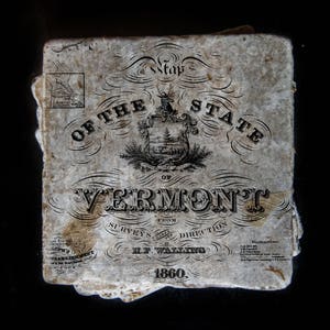 May include: Antique map of Vermont from 1860, featuring ornate lettering and a detailed state seal. The map, with a faded, aged appearance, includes text indicating the surveyor and publisher. The map's edges are slightly worn, adding to its vintage charm.