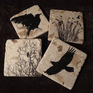 May include: Set of four square coasters made of beige marble with black silhouette images of crows and branches.