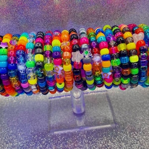 May include: A multi-colored bracelet made of numerous plastic pony beads in various shades including neon pink, green, blue, yellow, and orange. The bracelet features several translucent star-shaped beads interspersed throughout the circular design.