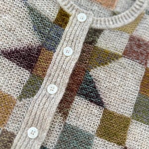 May include: A knit cardigan featuring a geometric checkerboard pattern in shades of beige, olive green, brown, and muted blue. The garment has a ribbed crew neckline, a vertical ribbed button placket, and four small white circular buttons.