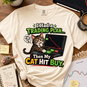 Może przedstawiać: Kremowy t-shirt z grafiką brązowego kota pręgowanego siedzącego przy laptopie z wykresem giełdowym spadkowym. Tekst brzmi: I Had a TRADING PLAN... OOPS... DID I DO THAT? Then My CAT HIT BUY. Projekt zawiera zielony i żółty napis.