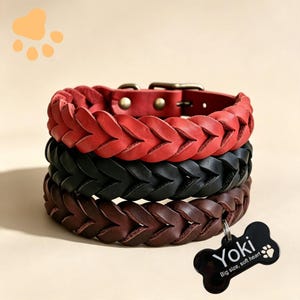 May include: Three braided leather collars in red, black, and dark brown stacked vertically. Each collar features a metal buckle and rivets. A black bone-shaped pet tag is attached to the bottom collar with the text Yoki and Big size, soft heart.