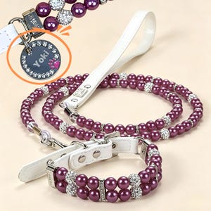 Könnte beinhalten: Ein Haustierhalsband und Leinen-Set mit doppelten Reihen violetter Perlen, durchsetzt mit silberfarbenen, kristallbesetzten Perlen. Das Set enthält einen weißen Lederriemen und eine runde, silberfarbene Metallmarke mit der Gravur Yoki.