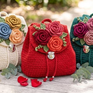 May include: Three crochet backpacks in cream, red, and dark green. Each bag features a flap decorated with three-dimensional crocheted roses in various colors, green leaves, and a silver-toned metal push-lock closure with drawstring cords.