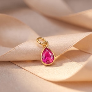 Op de afbeelding: Een druppelvormige hanger met een levendige, gefacetteerde roze edelsteen gezet in een gepolijste goudkleurige metalen zetting. De hanger is voorzien van een kleine, ronde goudkleurige ring aan de bovenkant voor eenvoudige bevestiging aan een ketting.