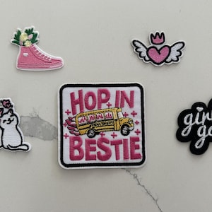 May include: A collection of five embroidered patches including a pink high-top sneaker with flowers, a pink heart with wings and a crown, two white cats, a square patch with a yellow bus and the text HOP IN BESTIE, and a black girl gang patch.