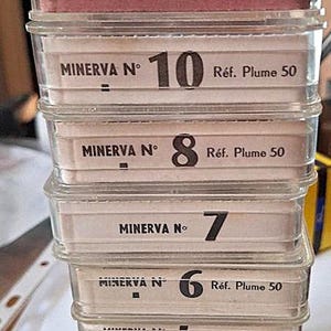 Könnte beinhalten: Ein vertikaler Stapel aus zehn durchsichtigen Kunststoffbehältern mit Schreibfedern, die jeweils mit dem Text MINERVA N, einer Zahl von 2 bis 16 und dem Text Réf. Plume 50 beschriftet sind. Die Behälter sind nach Größe absteigend sortiert.