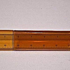 May include: A translucent amber-colored triangular scale ruler featuring black measurement markings along its edges. The ruler is composed of two segments joined together, displaying clear numerical increments for precise measurement tasks.