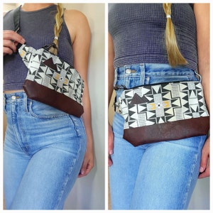 May include: A black and white geometric patterned fanny pack with a brown leather flap. The fanny pack is worn around the waist of a person wearing blue jeans.
