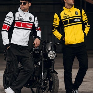 May include: Two jackets featuring Yamaha branding, one in white with red and black accents, the other in yellow and black. Both jackets display the text Semakin Di Depan, a 50th-anniversary emblem, and Yamalube logos on the chest and sleeves.