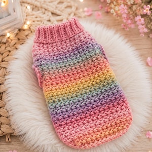 May include: A sleeveless pet sweater featuring a textured crochet stitch pattern with a gradient of colors transitioning from pink at the ribbed collar to yellow, green, and blue, ending in a soft pink hem along the bottom edge of the garment.