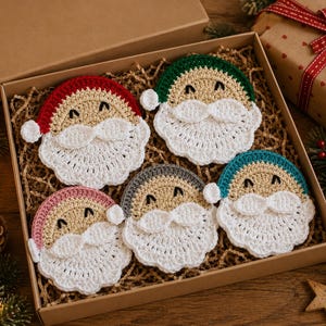 May include: A set of five circular crochet coasters shaped like faces with white beards and mustaches. Each coaster features a different colored hat: red, green, pink, gray, and teal. The faces are beige with black embroidered eyes and white pom-poms.
