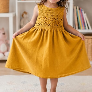 May include: A mustard yellow sleeveless dress featuring a crocheted bodice with a floral pattern and a solid, flared skirt. The upper section is crafted with intricate yarn work, while the lower portion consists of a smooth, plain fabric.