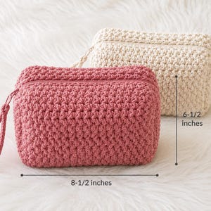 May include: A rectangular crochet pouch in dusty rose with a matching wrist strap and zipper, positioned in front of a cream-colored crochet pouch. The dusty rose pouch measures 8-1/2 inches in width and 6-1/2 inches in height as indicated.