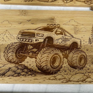 Può includere: Un tagliere rettangolare in bambù con un'illustrazione incisa al laser di un monster truck che guida su un terreno roccioso. Il disegno include montagne, pini, nuvole e nuvole di polvere, mettendo in risalto i grandi pneumatici del veicolo.