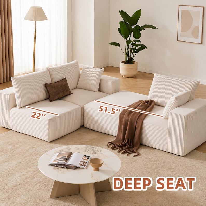 May include: A modular cream-colored corduroy sofa with a deep seat design. The sofa is composed of multiple sections, including a 22-inch wide piece and a 51.5-inch wide piece. It includes several matching throw pillows and a brown throw blanket.