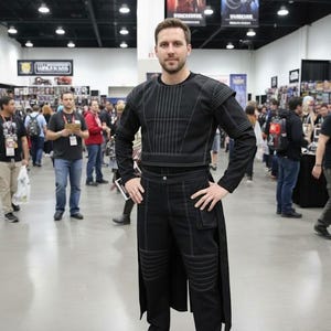May include: A black long-sleeved top and matching trousers featuring white contrast stitching. The top has vertical line detailing on the chest, while the trousers include reinforced knee panels, a small side pocket, and a long back panel extension.