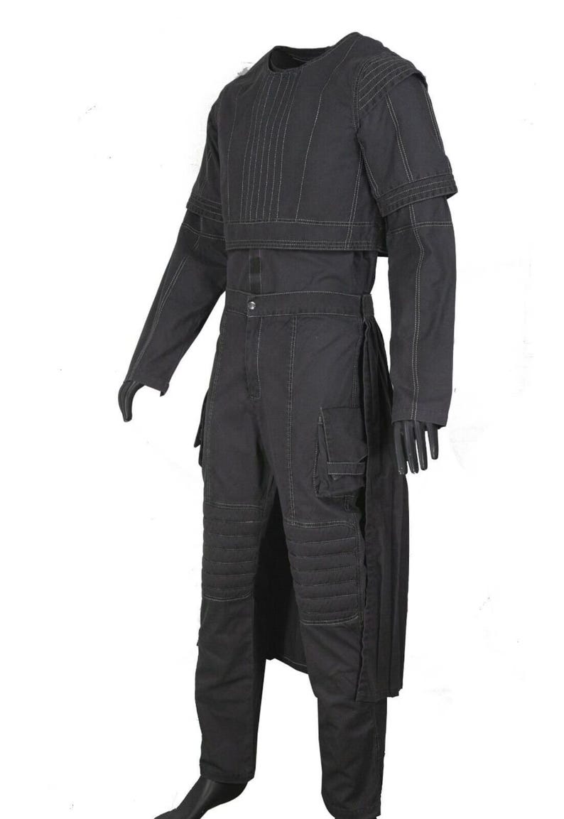 May include: A black long-sleeved jumpsuit featuring a cropped overlay top with vertical stitching, ribbed knee panels, and side cargo pockets. The garment includes a button-front closure at the waist and visible light-colored topstitching throughout.