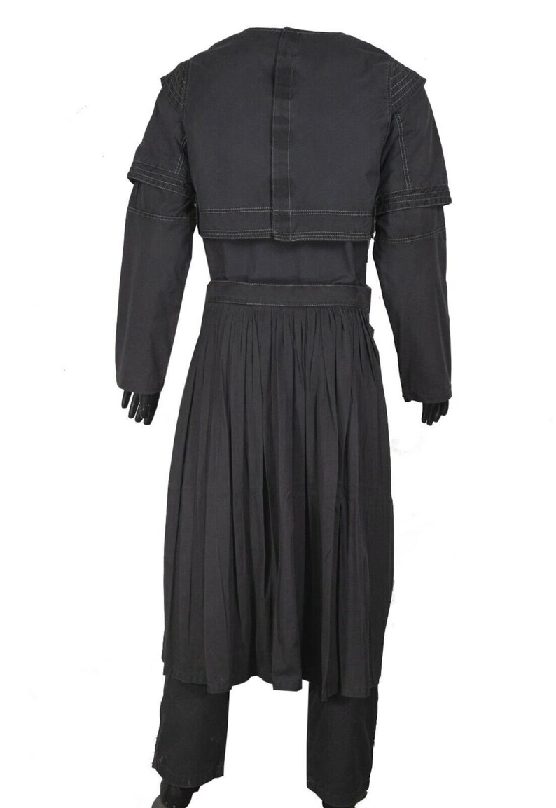 May include: A black long-sleeved coat featuring a structured shoulder cape overlay with visible stitching details. The garment includes a cinched waistline and a pleated skirt section that extends to the knees, paired with matching black trousers.