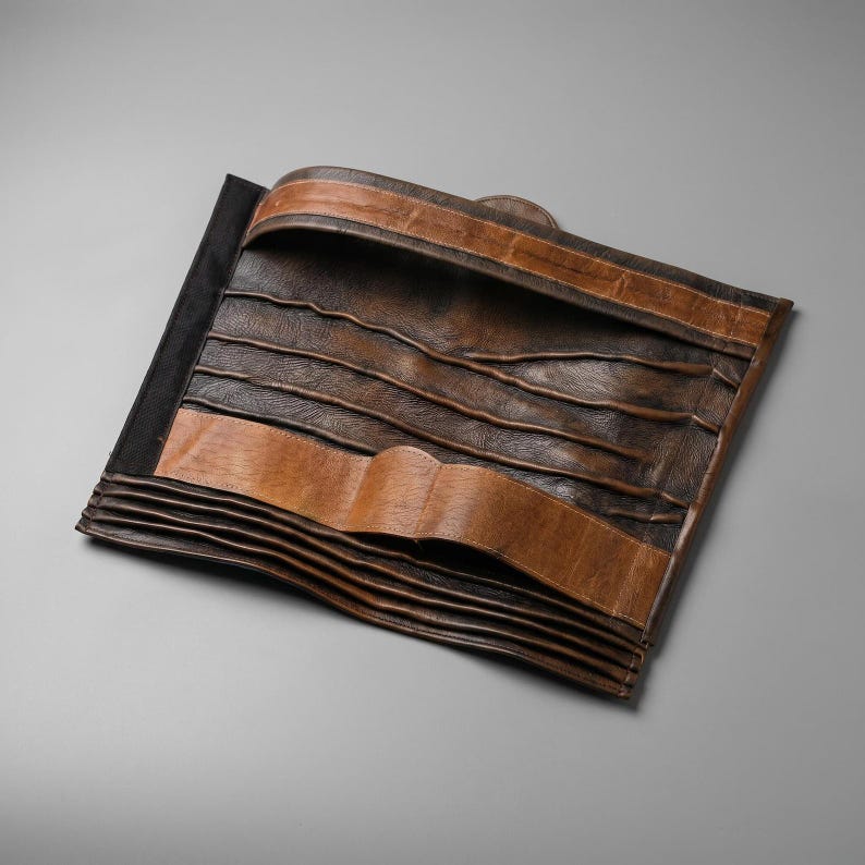 Peut inclure: Un organisateur rectangulaire en cuir pr&eacute;sentant une surface textur&eacute;e marron fonc&eacute; avec des poches cousues horizontalement. L'article comprend une bordure en cuir beige clair sur les sections sup&eacute;rieure et centrale, avec plusieurs fentes.
