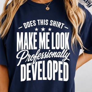 Peut inclure: Un t-shirt bleu marine à manches courtes avec le texte blanc imprimé : DOES THIS SHIRT MAKE ME LOOK Professionally DEVELOPED, accompagné de trois petites étoiles centrées entre la première et la deuxième ligne du motif graphique.