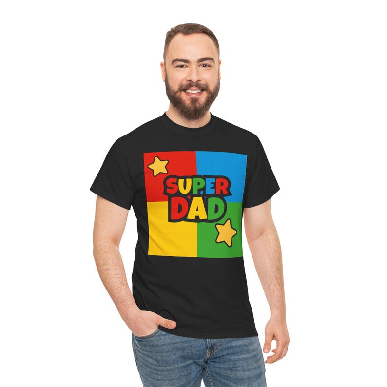 May include: Black t-shirt with a colorful graphic that says "SUPER DAD." The graphic is in a square divided into four sections: red, blue, yellow, and green. Two yellow stars are also included in the design.
