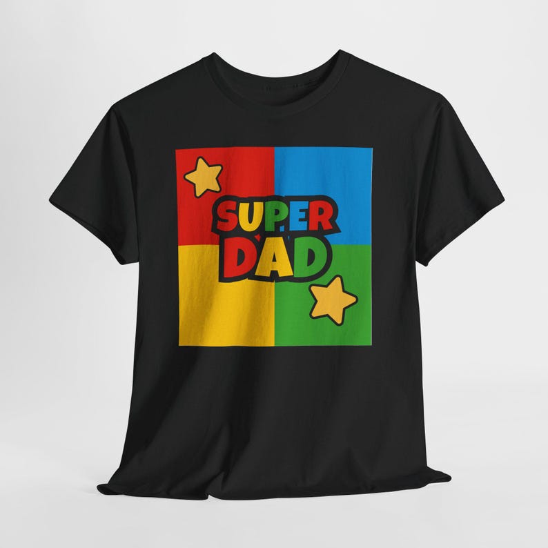 May include: Black t-shirt with a colorful graphic. The graphic features the words "SUPER DAD" in a bold font, set against a background divided into red, blue, yellow, and green squares. Two yellow stars are also included in the design.