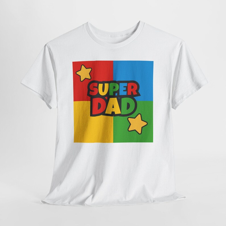 May include: White t-shirt featuring a colorful graphic that reads "SUPER DAD." The graphic is divided into four squares of red, blue, yellow, and green, with yellow stars in the corners. The text is in black and green.