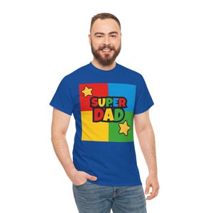May include: Royal blue t-shirt with a colorful graphic that says "SUPER DAD". The graphic is divided into four squares of red, blue, yellow, and green, with yellow stars on either side of the text.