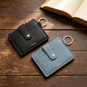 May include: A black and a dusty blue card holder, each featuring a scalloped top edge, a gold-toned snap button closure, and a gold metal keyring. The black holder is embossed with the name Owen, and the blue holder is embossed with the name Finn.