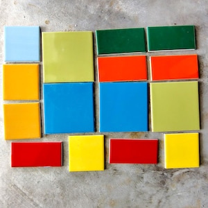 May include: A collection of fourteen ceramic tiles in various shapes and sizes, featuring a vibrant palette of colors including light blue, yellow, lime green, dark green, orange, bright blue, and red, arranged in a scattered, non-uniform layout.