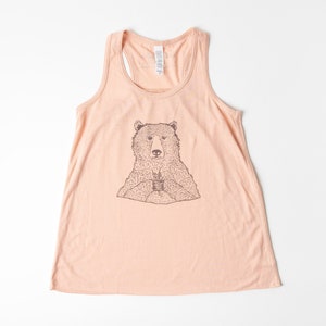 May include: A peach-colored tank top with a black and white illustration of a bear holding a cup.