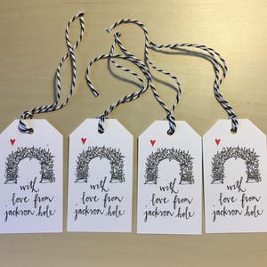 May include: Four white gift tags with black twine. Each tag features a black and white illustration of an archway with the text "with love from jackson hole" in black cursive.