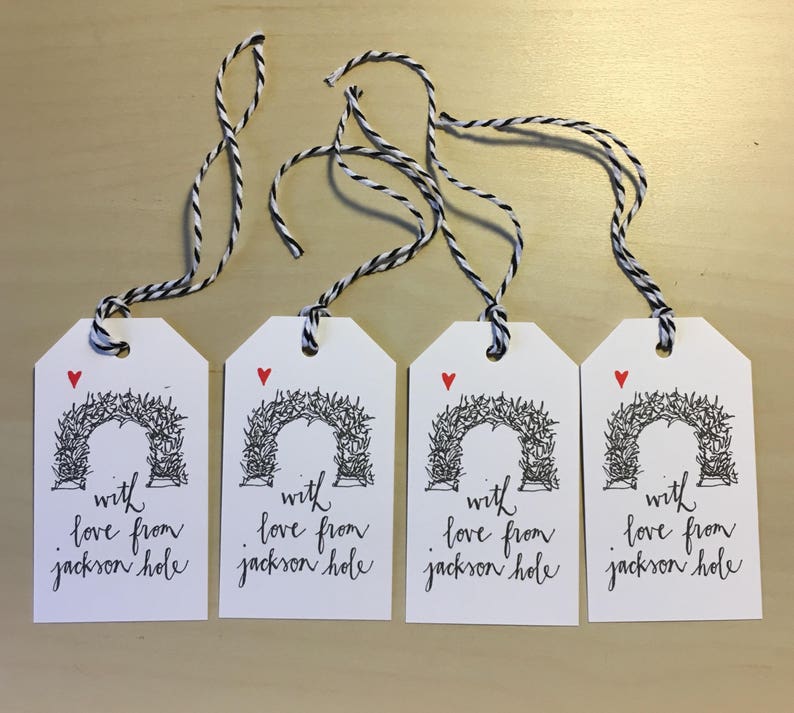 May include: Four white gift tags with black twine. Each tag features a black and white illustration of an archway with the text "with love from jackson hole" in black cursive.