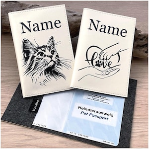 Könnte beinhalten: Zwei cremefarbene Reisepasshüllen mit schwarzen Aufdrucken. Eine Hülle zeigt eine Katzenillustration und das Wort Name, die andere eine Hand, die eine Pfote in einem Herz hält, mit dem Wort Love und Name. Ein Heimtierausweis ist sichtbar.