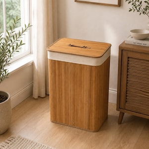 May include: A rectangular laundry hamper constructed from vertical bamboo slats with a natural wood finish. The hamper features a removable lid with a small brown leather handle and a wide band of off-white fabric trim around the top edge.