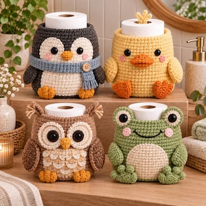 Puede incluir: Cuatro fundas de ganchillo para papel higiénico con forma de animales. La fila superior muestra un pingüino gris oscuro con bufanda azul y un pato amarillo. La fila inferior muestra un búho marrón y una rana verde con vientre crema.