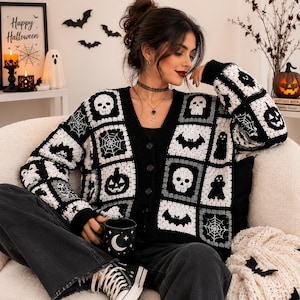 May include: A black and white crochet cardigan featuring a patchwork design of Halloween motifs including skulls, spider webs, bats, ghosts, and jack-o'-lanterns. The garment has a V-neckline, long sleeves, and a front button closure with dark buttons.