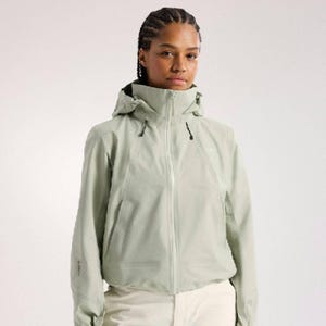 Könnte beinhalten: Hellgrüne Kapuzenjacke mit durchgehendem Reißverschluss. Die Jacke hat einen hohen Kragen und eine Kapuze mit Kordelzug. Die Ärmel haben ein dezentes Design. Das Model trägt eine weiße Hose. Die Jacke ist für Outdoor-Aktivitäten konzipiert.