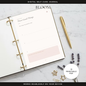 May include: A digital self-care journal titled BLOOM with a gold ring binder. The page features a gratitude section titled Three Good Things with lines for entries and a light pink box. A gold pen, two gold star clips, and lavender sprigs are present.