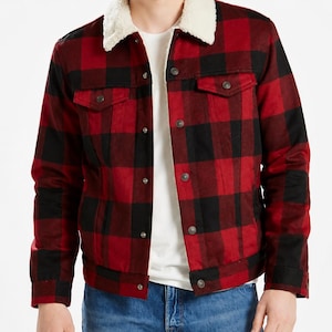 May include: A red and black buffalo check jacket featuring a white sherpa collar, long sleeves, and a front button fastening with metallic buttons. The jacket includes two chest pockets with buttoned flaps and is worn over a plain white t-shirt.