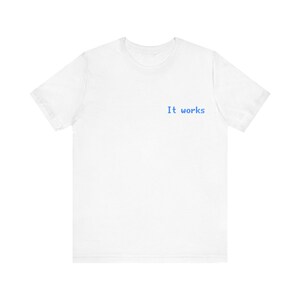 Op de afbeelding: Een wit t-shirt met de blauwe tekst "It works" op de voorkant. Het shirt heeft korte mouwen en een ronde hals. De stof lijkt een zacht, lichtgewicht materiaal te zijn.