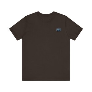 May include: A dark brown short-sleeved t-shirt featuring a small, light blue rectangular graphic on the upper left chest. Inside the light blue rectangle, the number 404 is printed in a dark brown font, creating a simple and clean design.