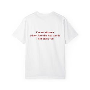 May include: A white short-sleeved t-shirt featuring dark red text printed on the back. The text reads: i'm not rihanna, i don't love the way you lie, i will block you. The garment has a crew neckline and a standard fit with short sleeves.
