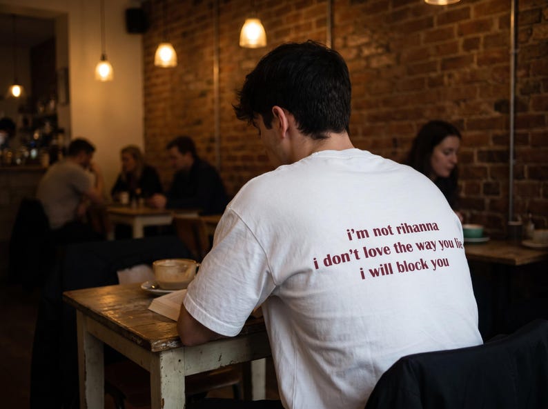 May include: A white short-sleeved t-shirt featuring dark red text printed on the back that reads: i'm not rihanna, i don't love the way you lie, i will block you. The shirt has a crew neckline and a standard fit, shown from the back view.