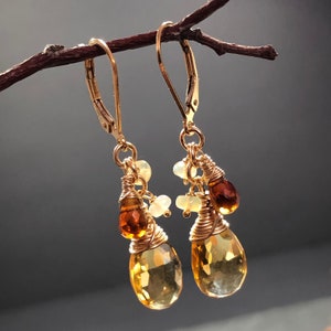 May include: Gold earrings featuring teardrop-shaped citrine and opal stones. The earrings are wire-wrapped and have a dangling design.