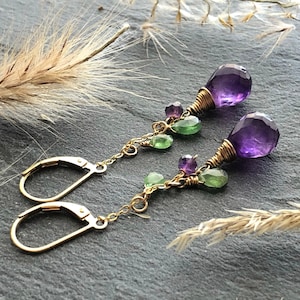 May include: A pair of dangle earrings with amethyst and green gemstones. The earrings are made with gold wire and have a hook closure.