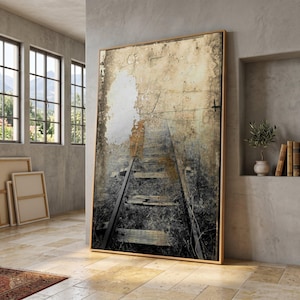 May include: Large framed artwork depicting a distressed image of railway tracks. The artwork has a neutral colour palette with shades of beige, brown, and grey. The wooden frame adds a warm tone. The artwork is leaning against a wall.