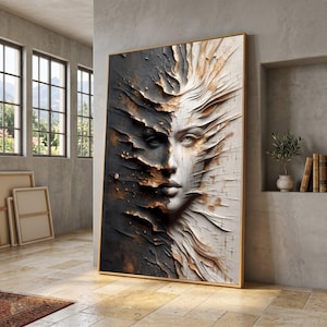 May include: A framed artwork depicting a split face portrait. One side is dark with textured details, the other is light with flowing lines. The artwork is displayed in a room with natural light and a neutral colour palette.
